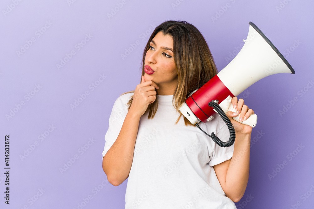 Young indian woman holding a megaphone isolated looking sideways with doubtful and skeptical expression. Young indian woman holding a megaphone isolated looking sideways with doubtful and skeptical expression.