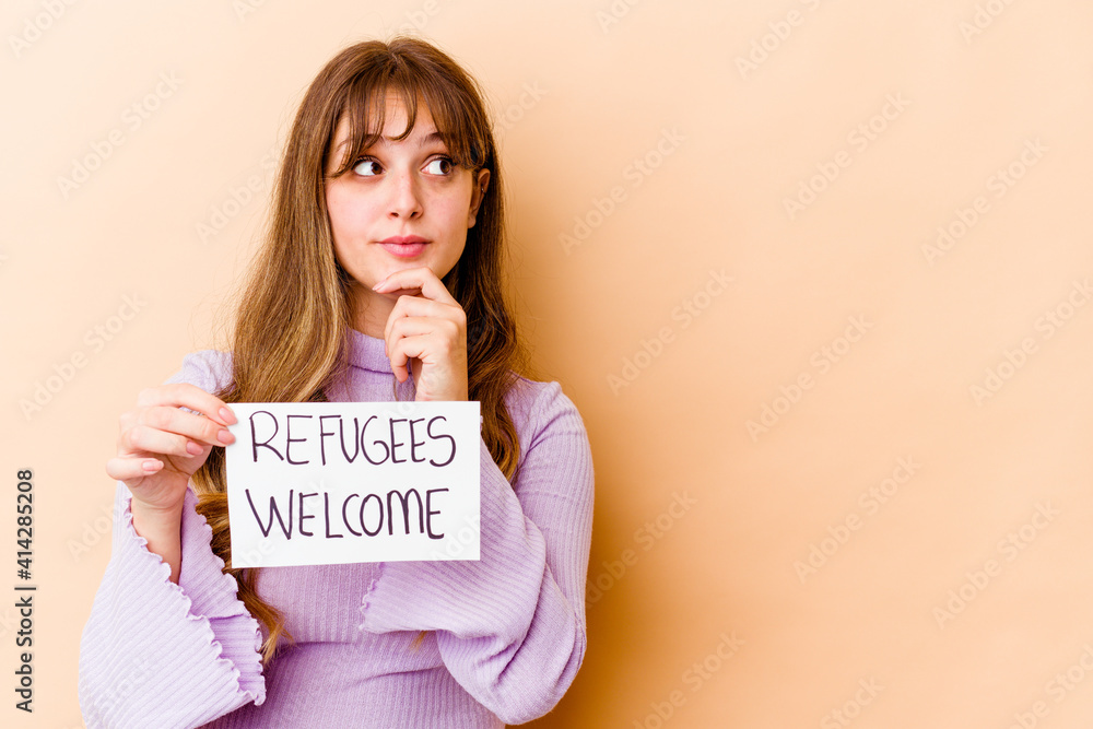 Young caucasian woman holding a Refugees welcome placard isolated looking sideways with doubtful and skeptical expression. Young caucasian woman holding a Refugees welcome placard isolated looking sideways with doubtful and skeptical expression.