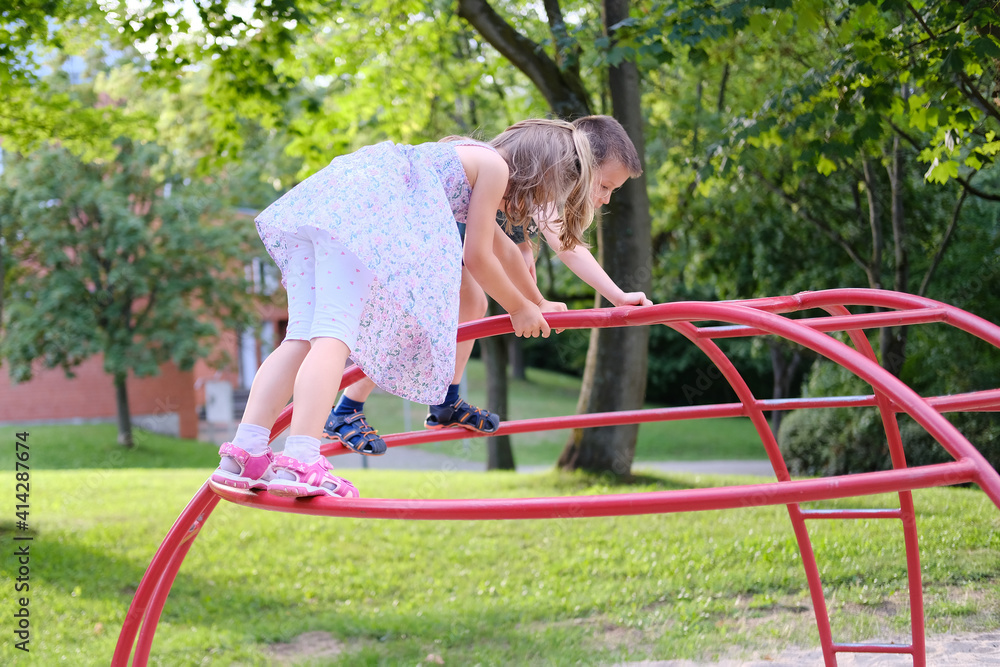 children walk in a summer park, a boy and a girl 6-7 years old in a dress climbs on a sports equipment on the playground, the concept of an active lifestyle, sports