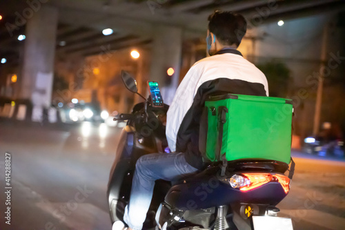 Motorcyclist with a green bag at the back on the way to deliver food. Fast food delivery service to customers