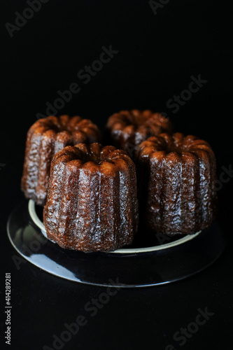 Caneles de bordeaux - traditional French sweet dessert serve with tea or coffee in dark tone on black background.