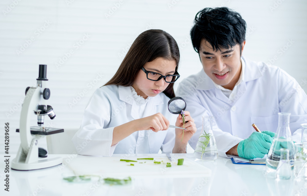 Little girl as young scientist use magnifying glass to analyze plant tissue and discuss with her teacher who sit near and consult the experiment also record the data in laboratory or classroom. Little girl as young scientist use magnifying glass to analyze plant tissue and discuss with her teacher who sit near and consult the experiment also record the data in laboratory or classroom.