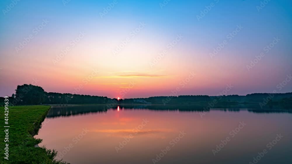 Lake view in park at sunrise, rising sun's reflection on water Lake view in park at sunrise, rising sun's reflection on water