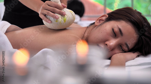 Young Asian woman getting relaxing during therapist put herbal spa ball on the back and massage in spa salon.