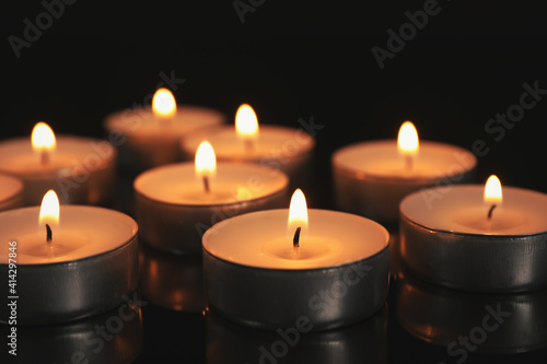 Many burning candles on black table in darkness