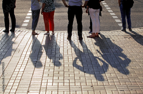 shadows of people waiting at a pedestrian crossing on summer evening, conceptual.