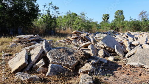 A large pile of slabs. Concrete debris from the old road demolition and left on the ground. On a green tree background and blue sky with copy space. Selective focus