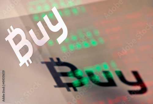 Word Buy with in form a bitcoin sign the same reflected inverted word on the background of glowing exchange rates on a window of a crypto bank office, in Kiev, Ukraine, on 22 October 2018.