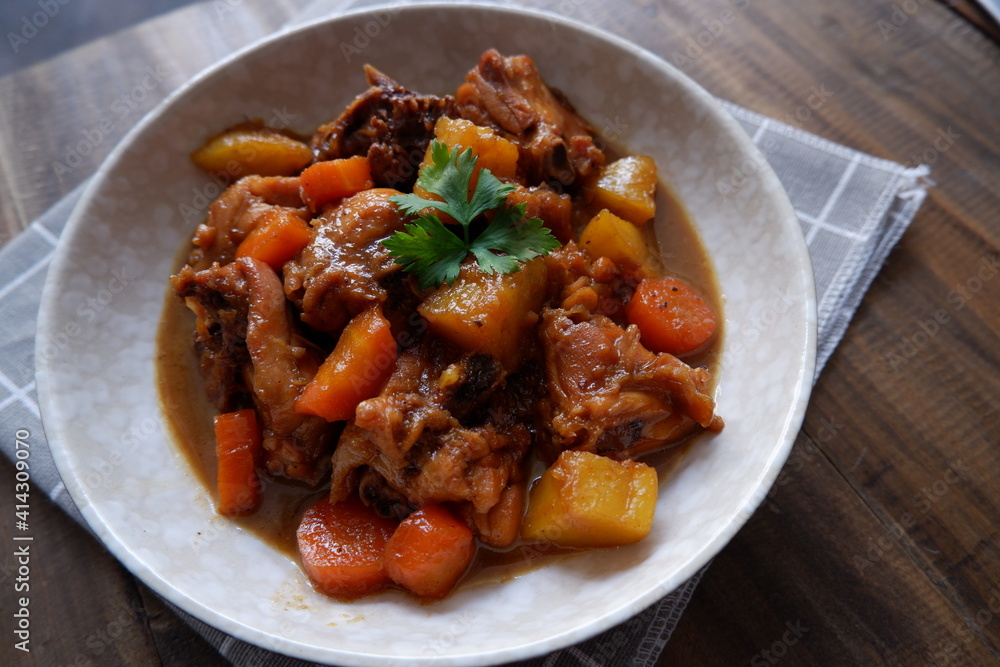 a plate of chicken stew with carrot and potato on a wooden table