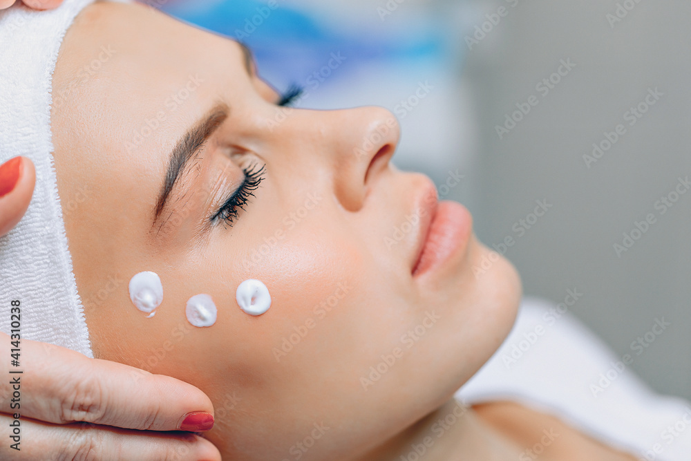 Close up woman's face with cream applied to cheekbones and cheeks after cosmetic procedures. Relaxation and rest. Cosmetology concept