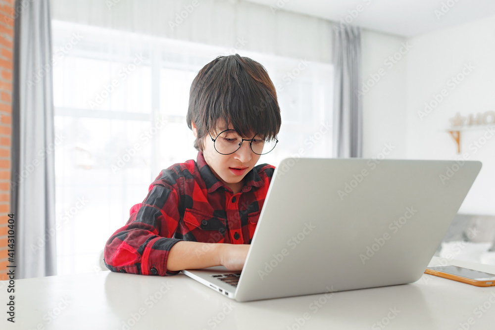 Kid boy with glasses learning at home on laptop for school. Adorable child making homework Kid boy with glasses learning at home on laptop for school. Adorable child making homework