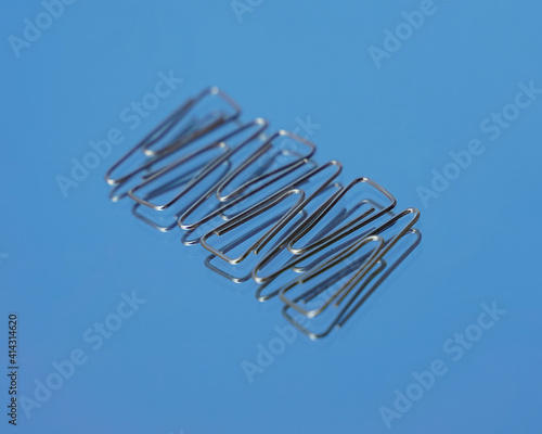 Realistic metal paper clip isolated on blue glass background. Page holder  binder. Realistic paper clip attachment with reflection of glass. paperclip. Attach business document files.