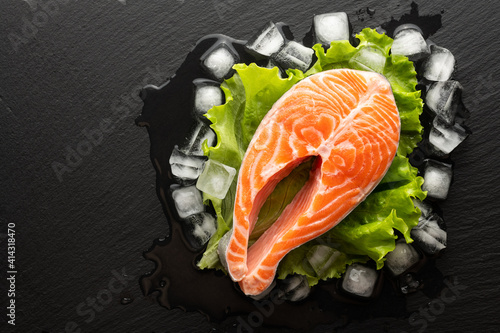 chilled salmon steak in lettuce and ice on a stone background, top view, place for text