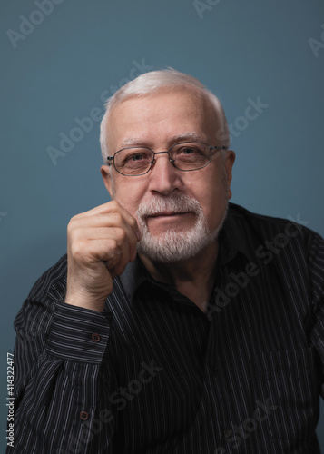 elderly handsome charismatic man sitting in glasses looking at the camera, studio, dark background, portrait