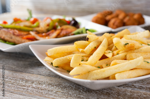 A view of a plate of french fries, featuring entrees in the background, in a restaurant or kitchen setting.