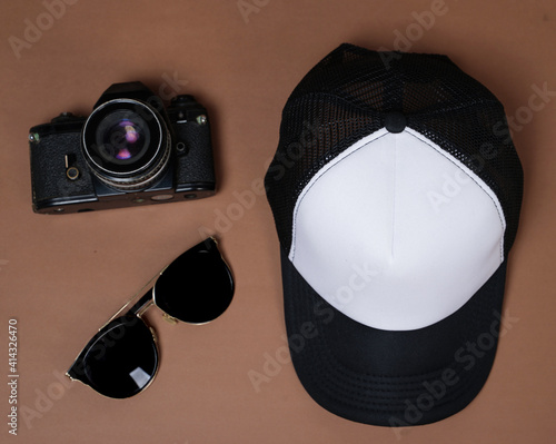 Blank baseball caps are used for design mockups. The hat on the side of an old camera and sunglasses. Plain hat isolated on brown background. Take a picture of a hat ready to be displayed. Mockup hat. photo