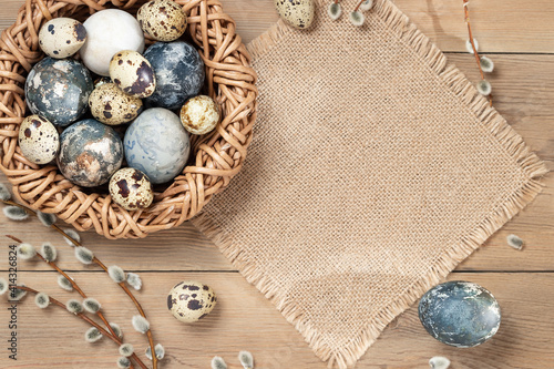 Easter composition - Easter eggs painted with natural dyes in a wicker nest on a wooden table, copyspace