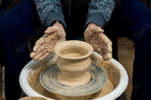 The woman potter's hands formed by a clay pot on a potter's wheel. The potter works in a workshop