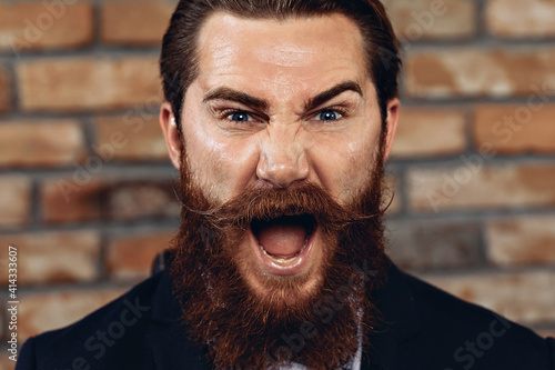 Portrait of a charismatic handsome man wearing a suit, hussar mustache and beard and posing against a brick wall. Concept os expression