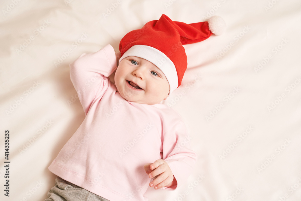 Cute small boy lying at bed. Childhood christmas concept. Light background. Smiling child. Xmas red hat. Copyspace. Stay home. Mockup. Pink female clothes Cute small boy lying at bed. Childhood christmas concept. Light background. Smiling child. Xmas red hat. Copyspace. Stay home. Mockup. Pink female clothes