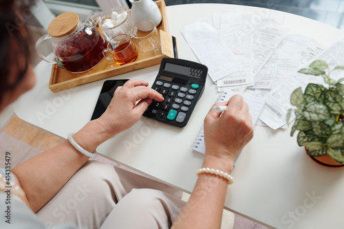 Hands of senior woman using calculator to check bills and sum up monthly expenses