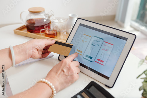 Hands of senior woman choosing subscription or payment plan on tablet computer and paying with credit card photo