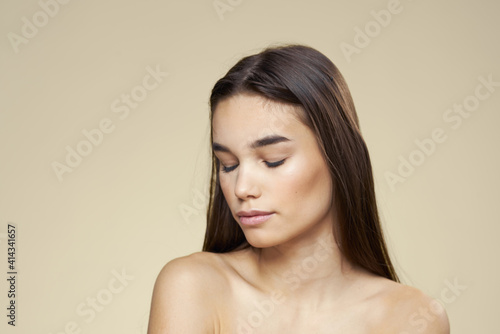 Woman with bared shoulders dark hair clean skin makeup beige background