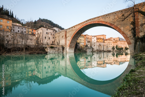 Wide angle view of the Devil's bridge in Fossombrone, mirrored on still water