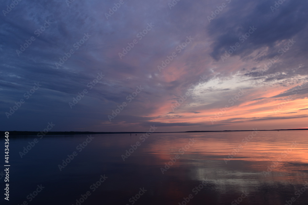 Cloudy sky in the  bright twilight light over the calm surface of the lake water