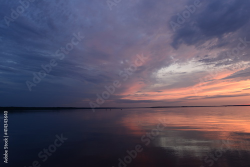 Cloudy sky in the bright twilight light over the calm surface of the lake water