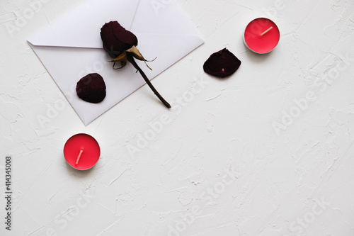 white envelope, dry rose and red candles on a white textured background