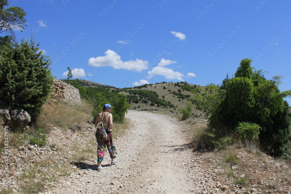 A girl traveler with a backpack walks along a mountain serpentine. Travel through the mountains of Crimea.	
