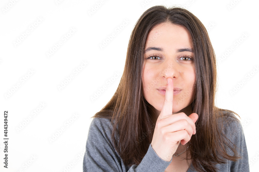 Close up of secret beautiful young woman showing shh silence gesture finger aside copy space blank white background Close up of secret beautiful young woman showing shh silence gesture finger aside copy space blank white background