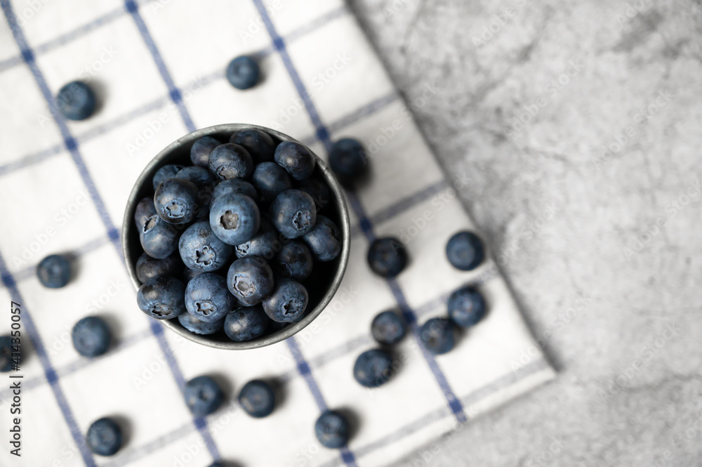 Fresh blueberries in a small metal bucket surrounded with some berries on a checked napkin. Top view. Rustic.