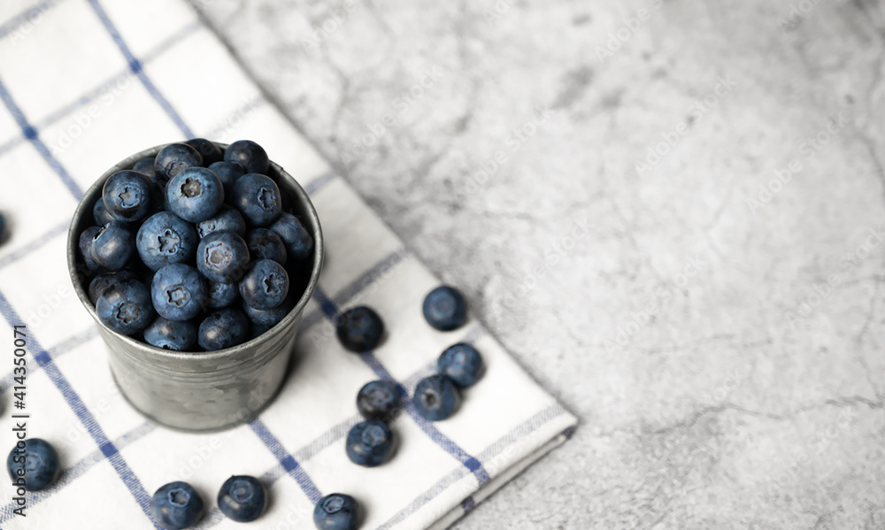 Fresh blueberries in a small metal bucket surrounded with some berries on a checked napkin. Top view. Rustic. Fresh blueberries in a small metal bucket surrounded with some berries on a checked napkin. Top view. Rustic.