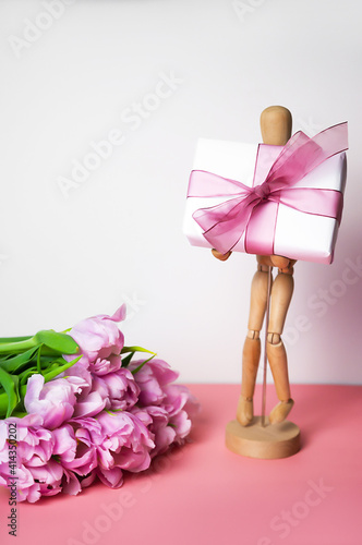 Close up of a bunch of tulips beside a wooden man holding a gift. Women's day, mother's day, birthday, anniversary concept. Shopping for holidays. Vertical card © piksik