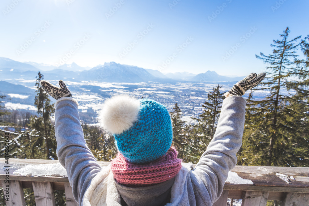 Fototapeta premium Happy young woman is raising her hands on the mountain, enjoying the view over Salzburg. Winter time on Gaisberg, Salzburg, Austria