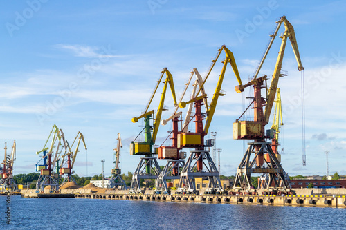 Many tall cargo cranes stand on the banks of the Venta River. Ventspils, Latvia, Baltic Sea. Copy space