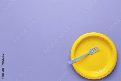 Plastic fork and plate on color background