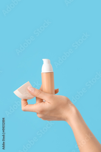 Hand with makeup sponge and concealer on color background