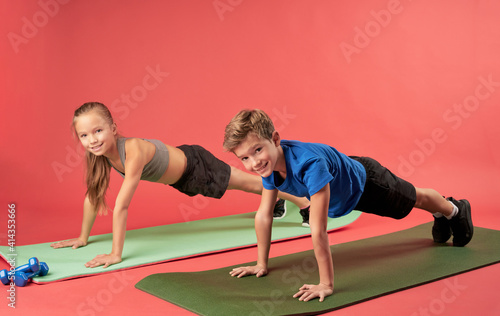 Joyful kids doing plank exercise against red background