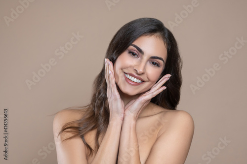 Woman with bare shoulders touching her palms to face