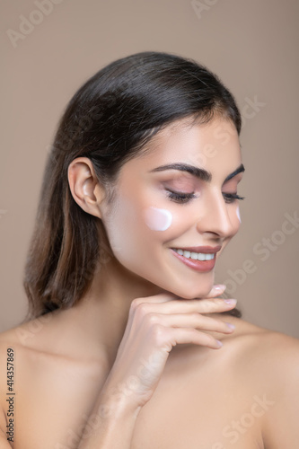 Woman with bare shoulders with cream on her cheek
