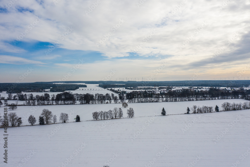 Winter landscape in Germany from a bird's eye view, with snow-covered fields, leafless trees and wind turbines Winter landscape in Germany from a bird's eye view, with snow-covered fields, leafless trees and wind turbines