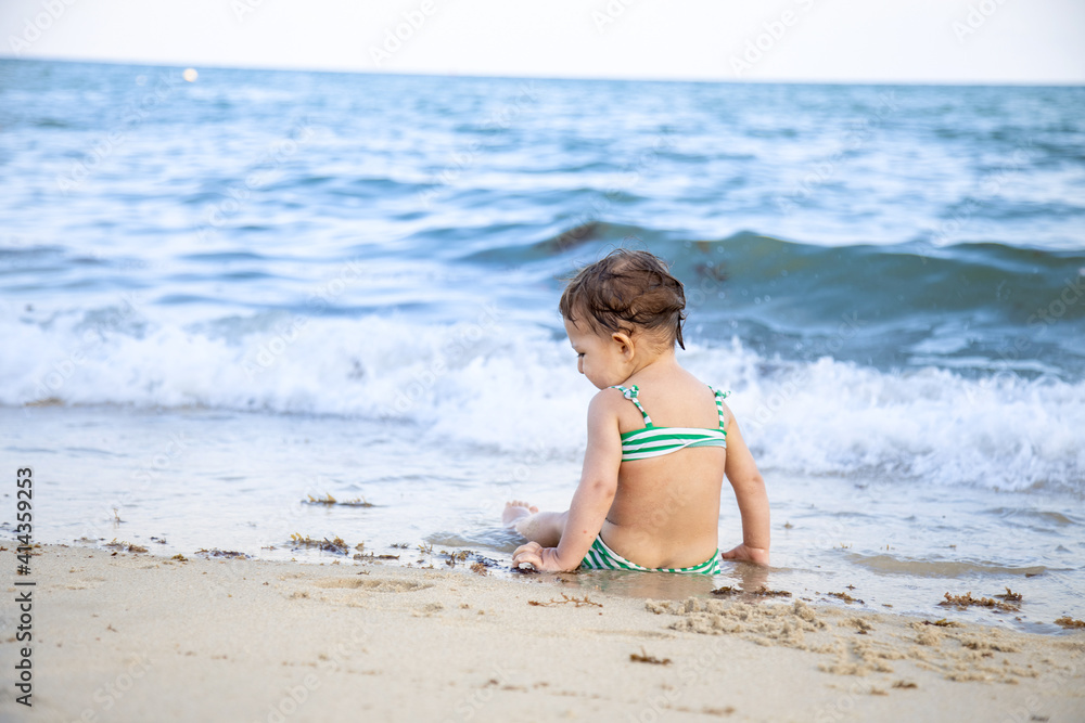 little toddler girl sitting on the beach and looking at the waves. back view little toddler girl sitting on the beach and looking at the waves. back view