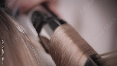 Very close-up of the curling iron for curling hair with blonde hair. High quality 4k footage