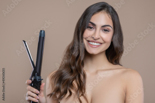 Pretty woman with bare shoulders with curling iron