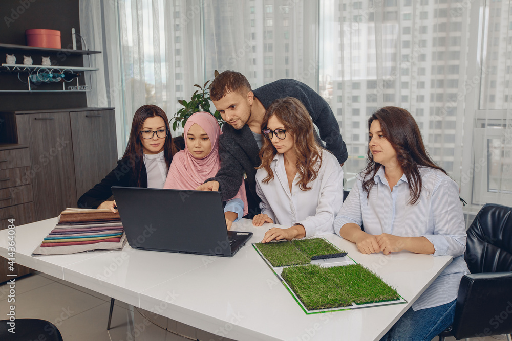 Professional attractive group of promising office workers analyzing and working on a project. Lovely woman in a pink hijab in the office. Multi-religious team. Team work concept Professional attractive group of promising office workers analyzing and working on a project. Lovely woman in a pink hijab in the office. Multi-religious team. Team work concept