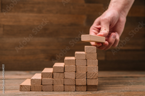 Business concept - hand builds a ladder from wooden blocks. Driving business at the peak concept.