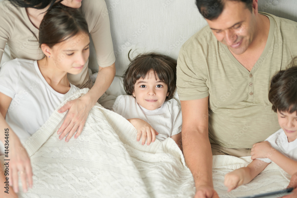 Portrait of cute little latin boy smiling at camera while spending time with his siblings and parents, staying in bed in the morning Portrait of cute little latin boy smiling at camera while spending time with his siblings and parents, staying in bed in the morning